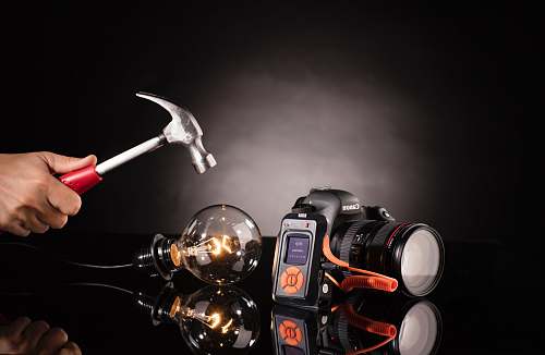 cell phone person holding claw hammer beside bulb and DSLR camera computer